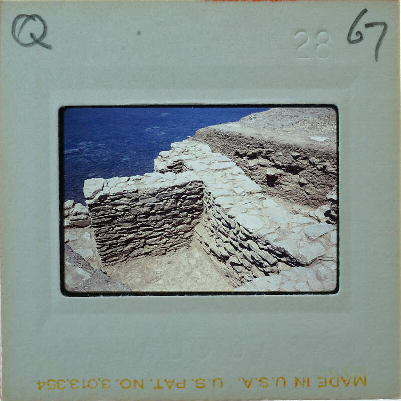 A photograph of a stone structure, possibly ruins, overlooking the ocean with a film strip label at the bottom.