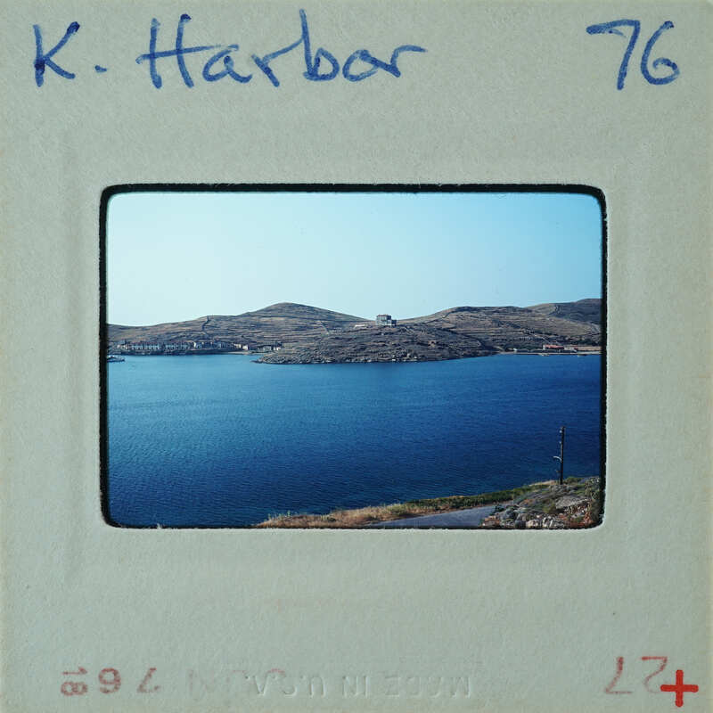 A vintage photograph of a serene harbor with calm waters and distant mountains.