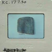A small, dark blue rock on a white surface with a label and date stamp.