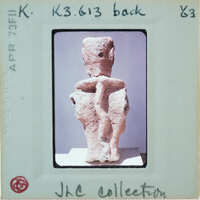 Ancient clay figurine with a humanoid shape, showing back with braids.