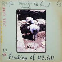 Two archaeologists working at a dig site, with handwritten notes on the photo.