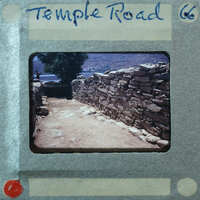 Stone wall with a dirt path and trees in the background.