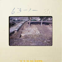 Ancient ruins with stone columns and walls, partially covered by dirt and vegetation.