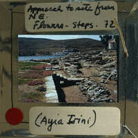 A photograph of an archaeological site with ruins and a body of water, accompanied by handwritten notes on a label.