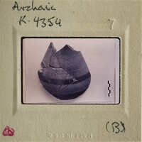 A photograph of an ancient artifact, possibly a pottery shard, with visible cracks and texture.