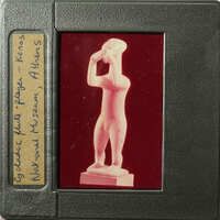 A photograph of an ancient Greek statue on display, taken from behind glass.