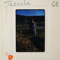 A vintage photo of a person standing on a rocky surface with mountains in the background.