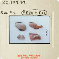 Old ceramic shards on white surface with handwritten notes and numbers.