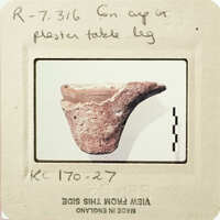 Ancient artifact, possibly a bowl or cup, with visible wear and tear, displayed on a white surface.