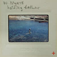 A vintage photo of a person swimming near rocks with blue water, labeled "W. MYERS HOLDING TETHER".