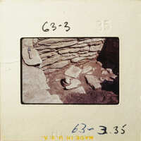 Old photograph showing an excavation site with stone ruins and a tool, possibly a chisel.