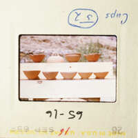 A photograph of a white wooden table with several clay pots on top, placed outdoors.