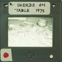 A black and white image of a cluttered table with various ceramic objects on it.