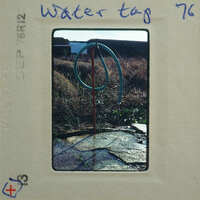 Water hose attached to a spigot with water dripping from it, set against a grassy background.