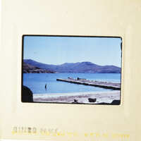 This photo shows a serene beach scene with a dock and mountains in the background.