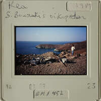 A person standing on rocky terrain overlooking water, with mountains and sky in background.