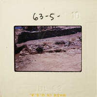 Old photograph of a stone wall with vegetation and dirt ground.