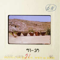 A photograph of an old film slide with a desert landscape and four small clay pots on a wooden surface.