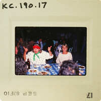 Two women sitting at a table with food, smiling and giving thumbs up. Catalog number KC.190.17