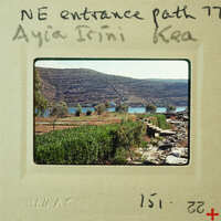 A vintage photo of a rocky coastline with mountains and vegetation, labeled as "NE ENTRANCE PATH AYIA RINI KEA" on the border.