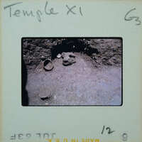 Stone wall with niche at bottom and pottery on the floor.