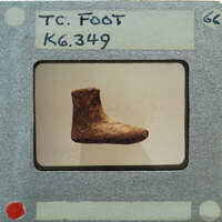 An old, worn-out leather boot on display with a label and number attached to it.