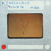 Red and gold necklace on a display stand with labels.