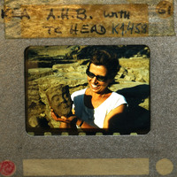 Woman holding terracotta artifact (K1.458) with smile, set against rocky background.