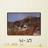 A photograph of an ancient stone wall with vegetation on top, set against a clear sky.