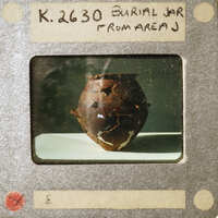 Photograph of a burial jar with handwritten label and identification number.