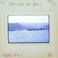 A vintage photograph of a serene bay with calm waters and distant mountains, enclosed within an album page.