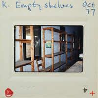Empty wooden shelves inside a building, captured on a Polaroid photo with handwritten notes.