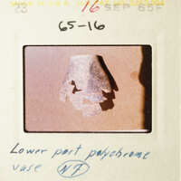 This is a photograph of an old slide featuring a microscope slide with a small, blurry object on it, which appears to be a piece of metal or plastic with a jagged edge and a hole in the center, placed against a white background