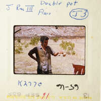 A man holding a cup in front of a tree and a building.