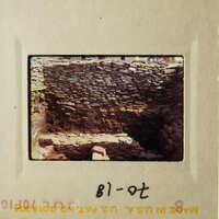 The photo shows an ancient stone structure, possibly ruins, with a rock wall and a dirt floor.