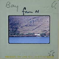 A vintage photograph of a scenic bay with mountains and water, featuring handwritten notes on the border.