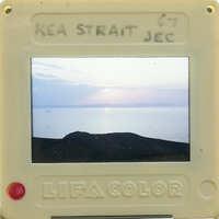 A small camera displaying a photo of a sunset over water with mountains in the background.