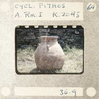 An old clay pot sitting on the ground with a stone wall in the background.