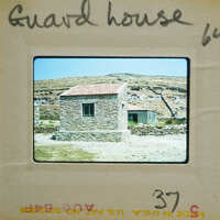 Old stone guard house with a red roof, set against a mountainous landscape.