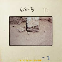 This is an image of a photograph depicting a close-up view of what appears to be archaeological excavation, possibly showing layers of earth and artifacts.