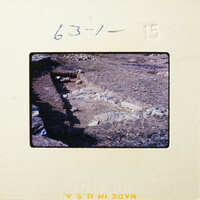 Ancient ruins with stone walls and foundations partially uncovered on a dirt field.