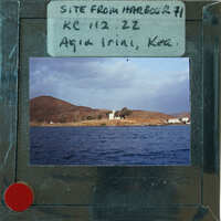 A view of a coastal town with buildings, a churche and mountains from the water.