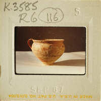 Ancient-looking ceramic vase with visible cracks and imperfections, photographed on a light surface.