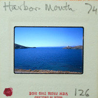A vintage photograph of a serene harbor with calm waters and distant hills, mounted on an old film strip.