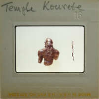 Small figurine of a man, possibly from ancient civilization, displayed on white background within a film strip frame.