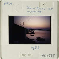 Sunset over calm water with boats and distant hills.