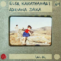 A vintage photo of a child standing on rocks with mountains in the background, labeled "Elsa Karathanasi" and "Adriani Daka."