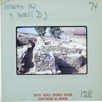 Stone ruins of an ancient structure, possibly a wall or tower, with trees and water in the background.