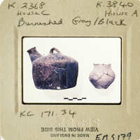 Two ancient vases, one intact and one broken, displayed on a white surface with labels.