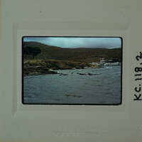 A photograph of a rocky coastline with water and mountains, enclosed within an old film negative frame.